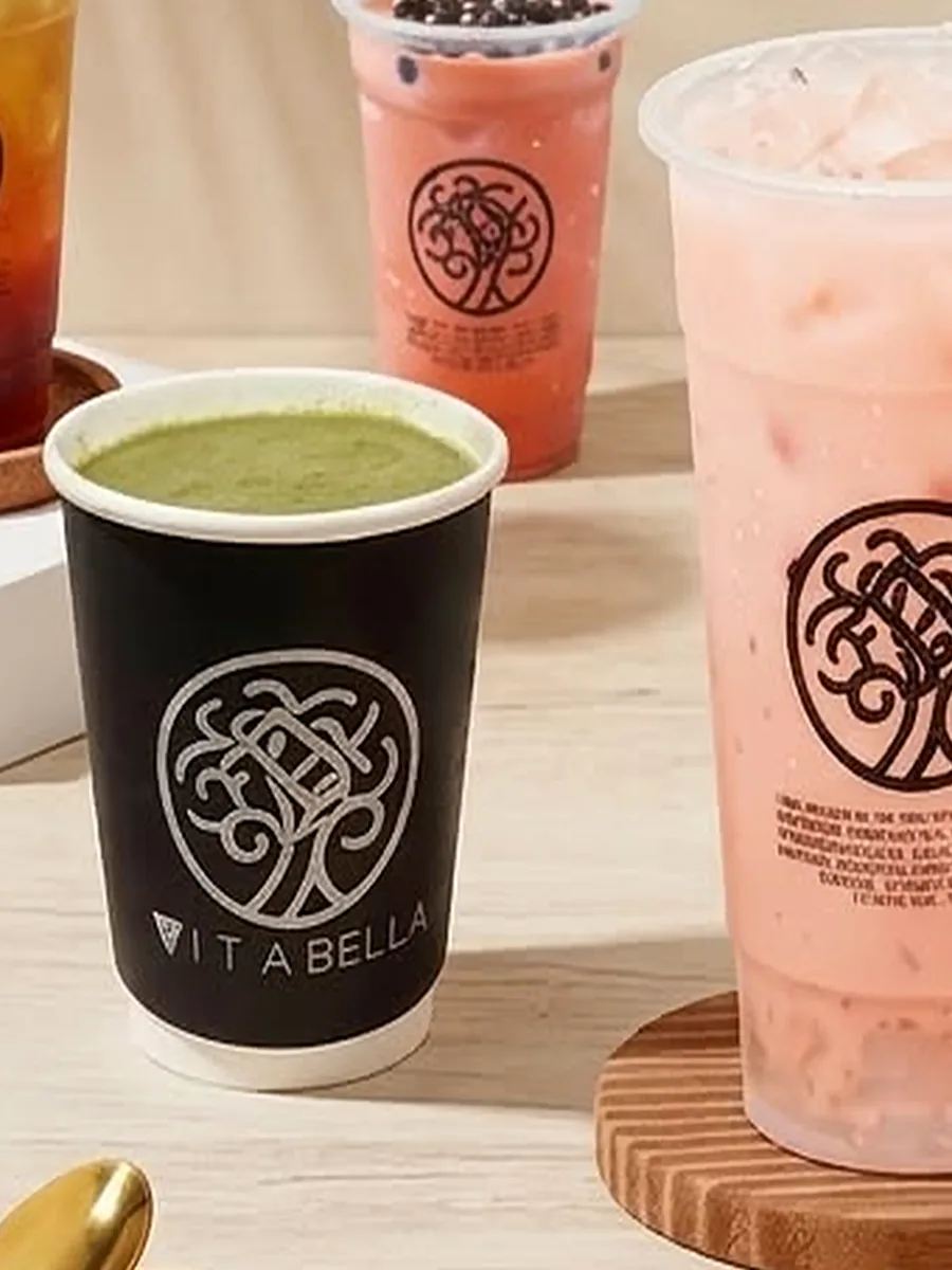 Hot matcha in a black Vita Bella cup beside an iced pink milk tea
